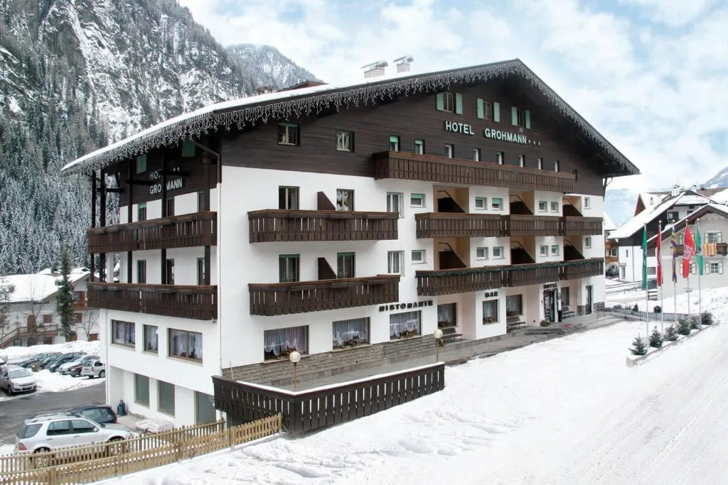 Hotel Grohmann in inverno con neve, balconi in legno e bandiere sotto il cielo nuvoloso