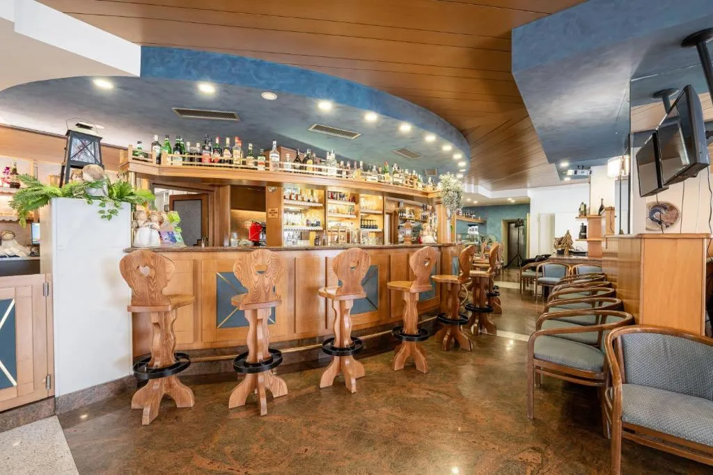 Bar dell'hotel con bancone in legno, sgabelli intagliati e soffitto blu con illuminazione