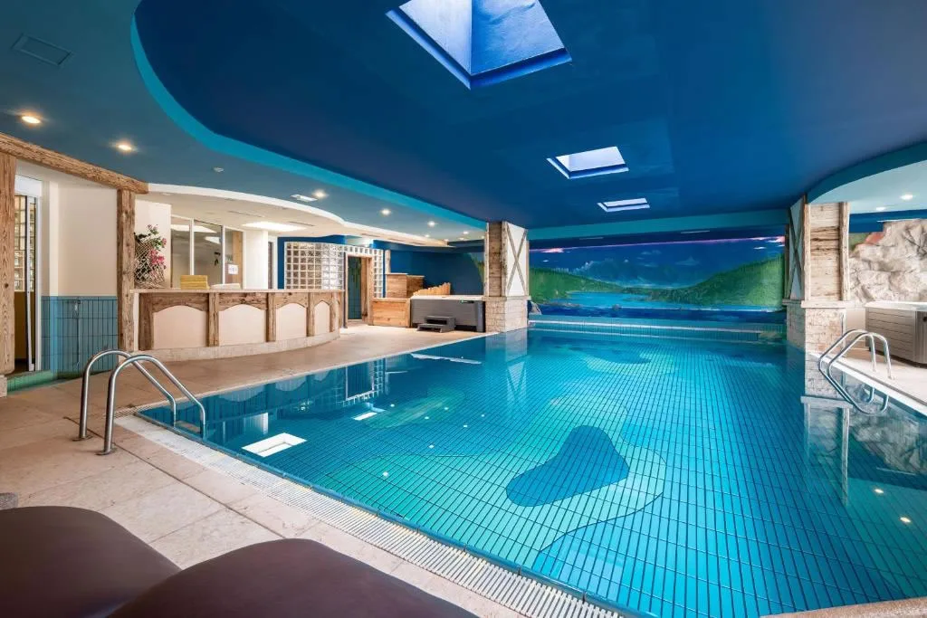 Piscina coperta con acqua azzurra, soffitto blu con lucernari e murale panoramico