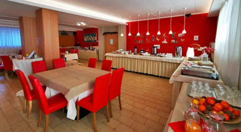 Sala colazioni con tavoli apparecchiati, sedie rosse, buffet e parete rossa