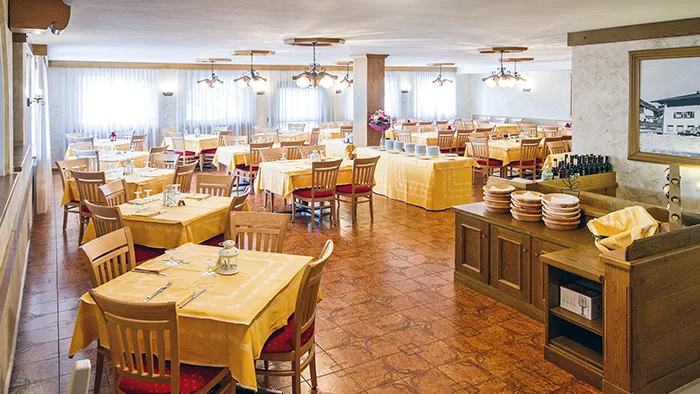 Sala ristorante ampia con tavoli in legno, tovaglie gialle e illuminazione tradizionale
