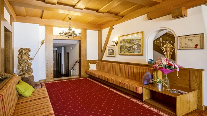 Hall in stile alpino con panche in legno, tappeto rosso e soffitto travi a vista