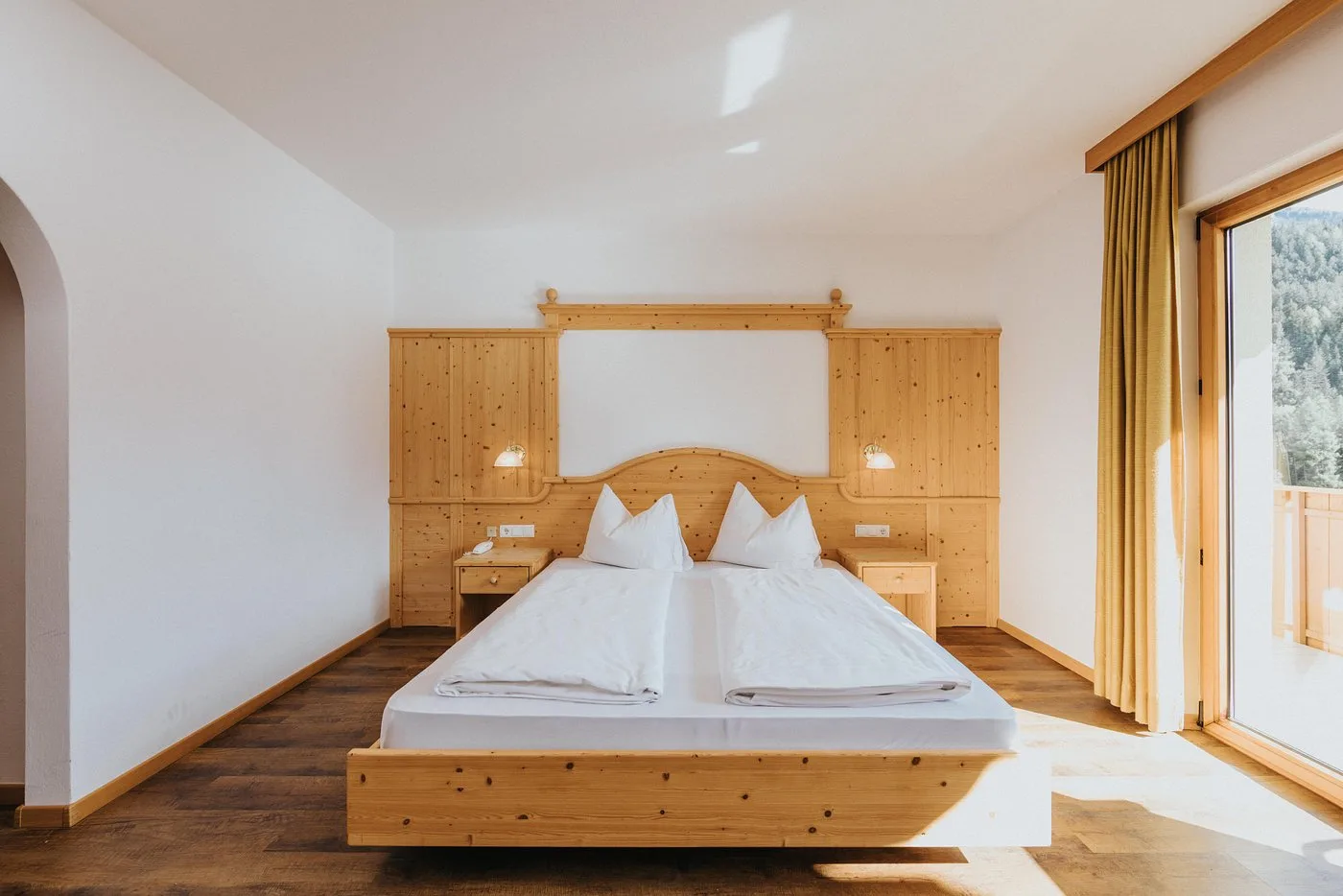 Camera luminosa con letto matrimoniale in legno di cirmolo e vista sui boschi