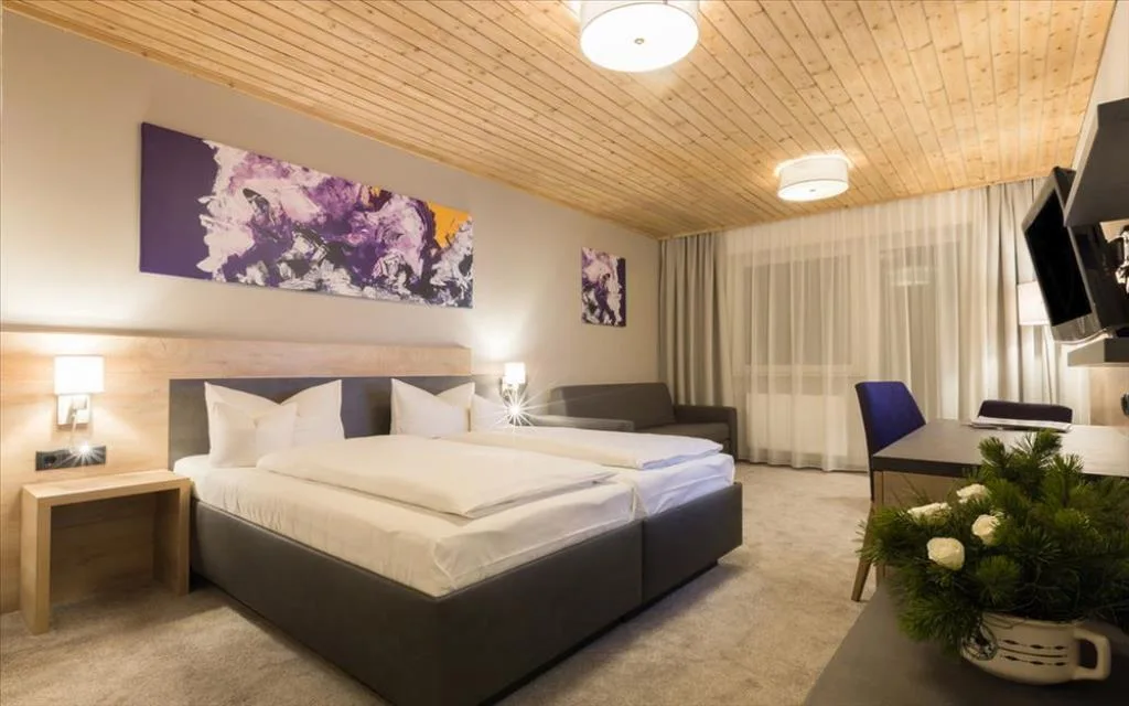 Camera con letto matrimoniale, divano, quadri astratti e soffitto in legno