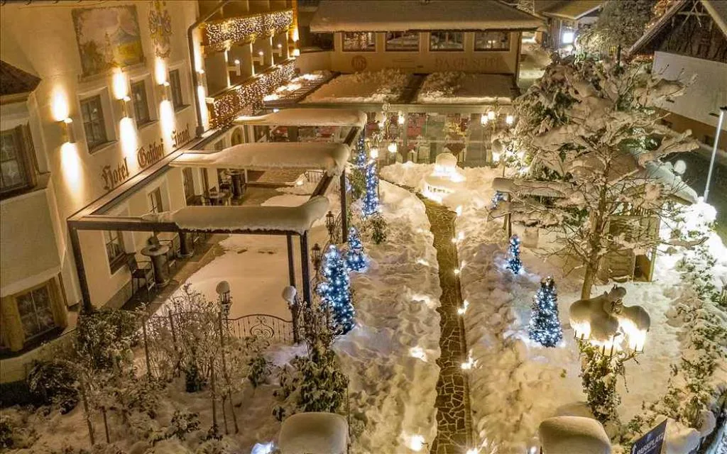 Cortile innevato dell'hotel illuminato di sera con alberi decorati e luci natalizie