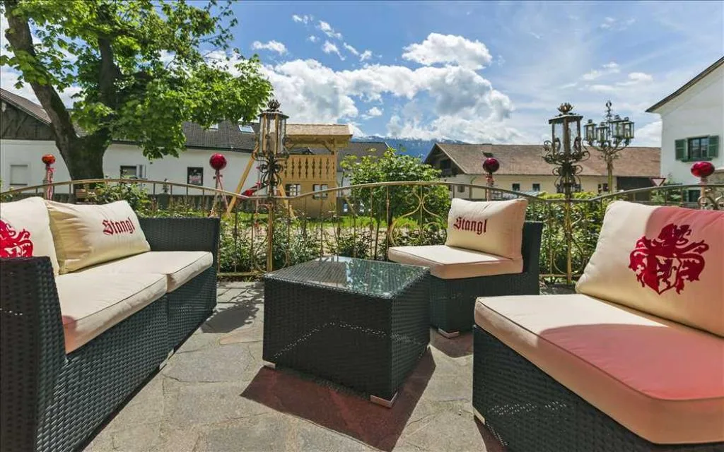 Area lounge esterna con divani in rattan, cuscini con logo Stangl e vista sulle montagne