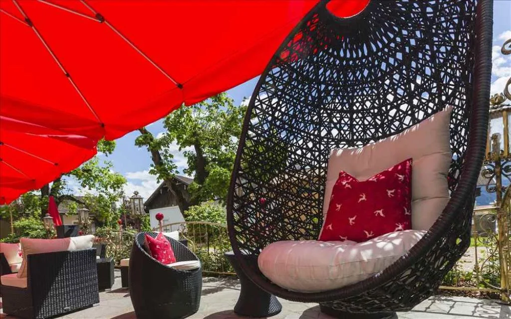 Dettaglio della terrazza lounge con poltrona sospesa in rattan e cuscini rossi