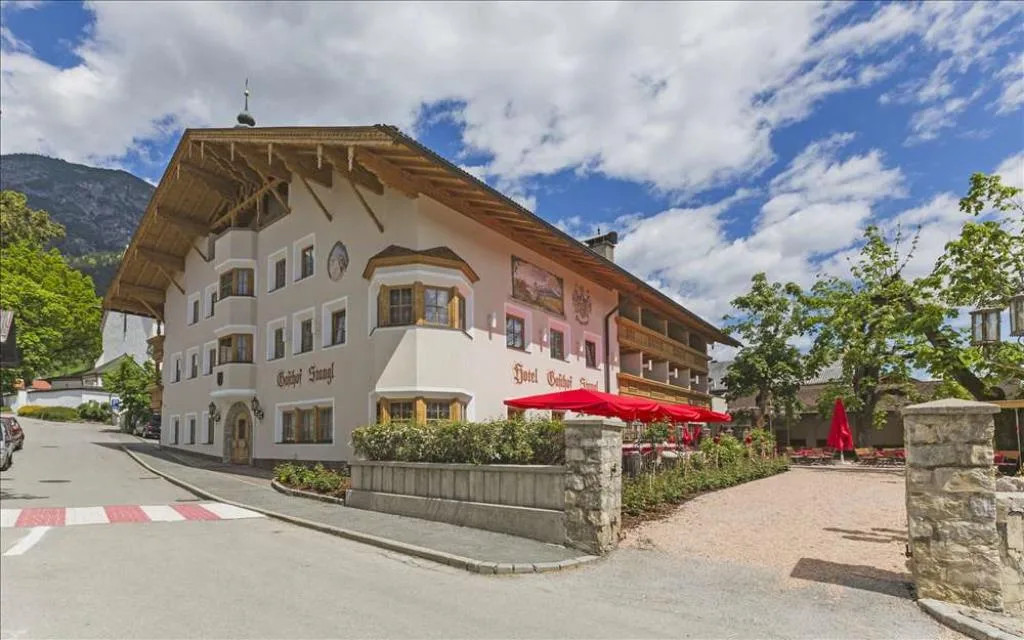 Facciata dell'hotel in stile tirolese con ampio tetto in legno e terrazza con ombrelloni rossi