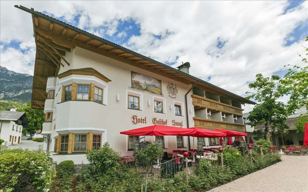 Esterno dell'hotel con affreschi, stemma, terrazza con ombrelloni rossi e giardino