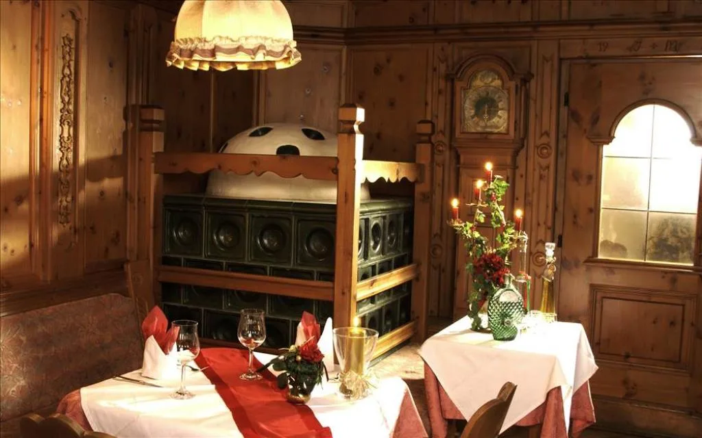 Angolo intimo del ristorante con stufa in maiolica verde, boiserie in legno e tavoli apparecchiati