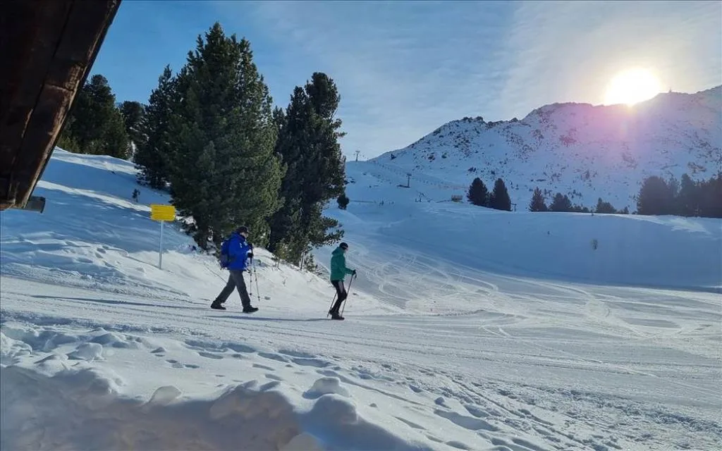 Escursionisti con racchette da neve su una pista innevata al tramonto tra le montagne