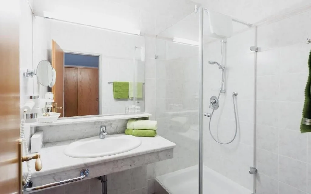 Bagno bianco con doccia, lavabo e asciugamani verdi
