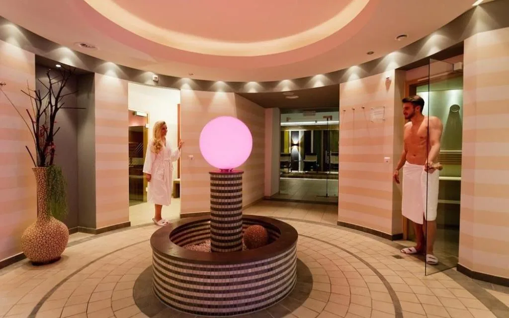 Area sauna con fontana luminosa rosa e due persone in accappatoio