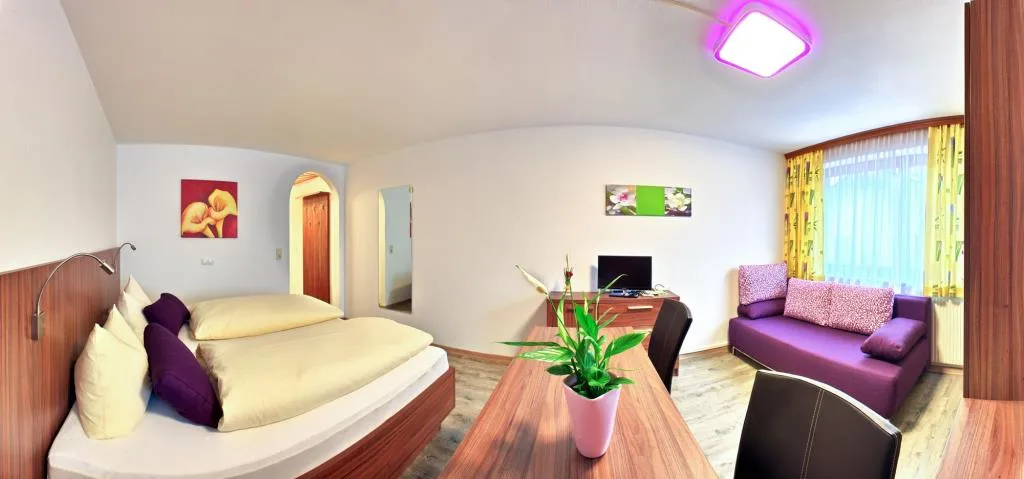 Vista panoramica di una camera con letto matrimoniale, divano viola e area soggiorno