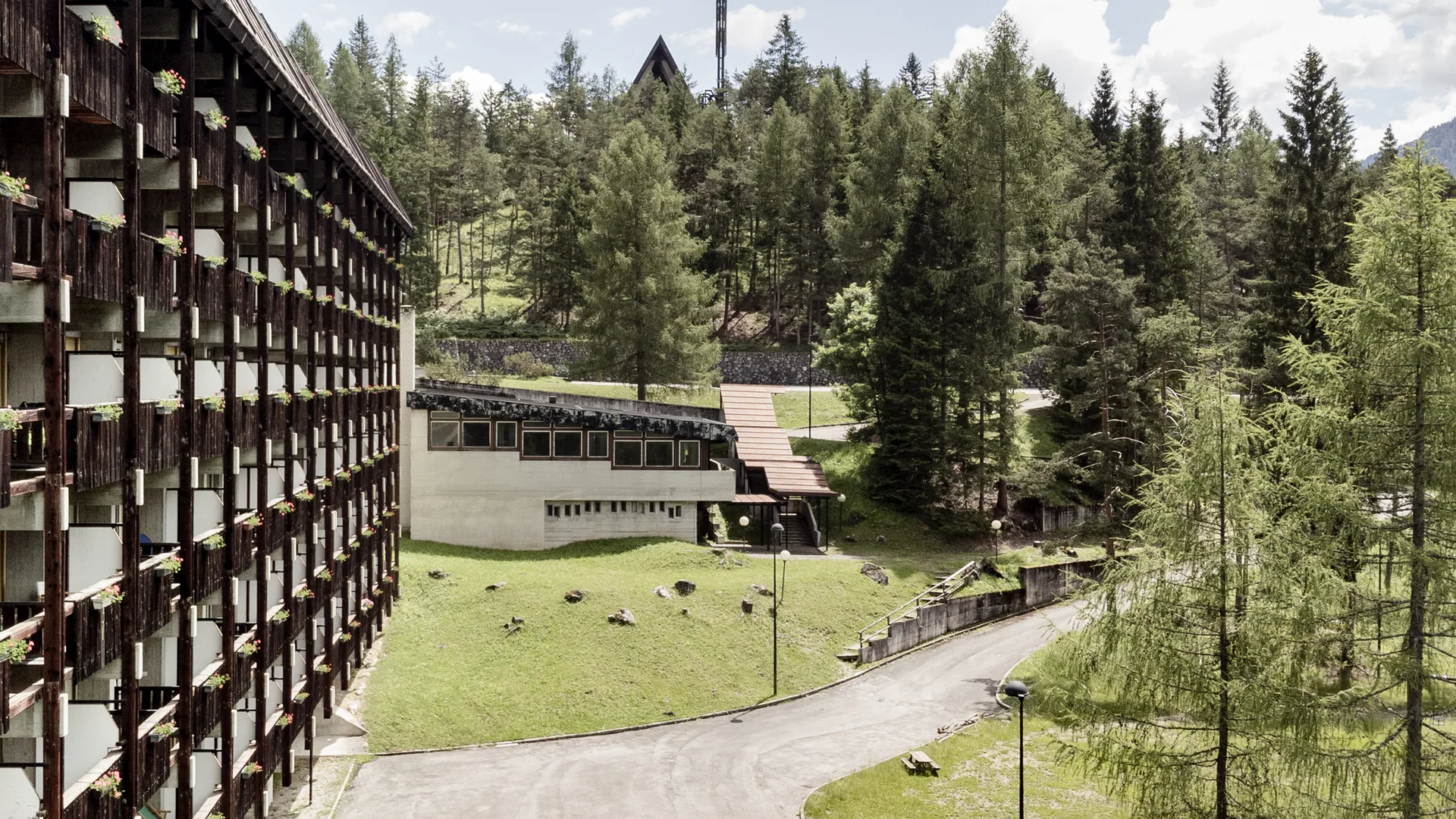 Esterno dell'hotel con balconi fioriti immerso in un bosco di conifere