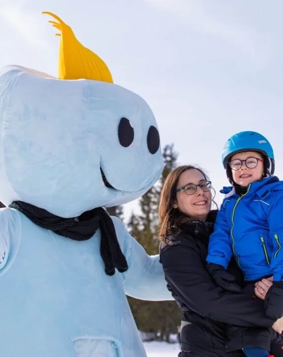Mamma e bambino sorridenti accanto alla mascotte dell'hotel sulla neve