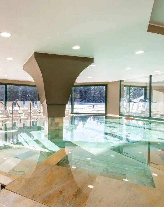 Piscina interna con acqua turchese e vista sui boschi innevati