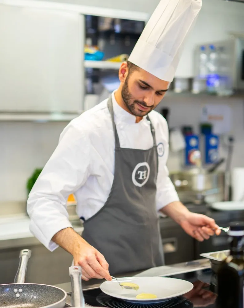 Chef giovane in un moderno ristorante, mentre impiatta un piatto con cura su un tavolo di cucina.