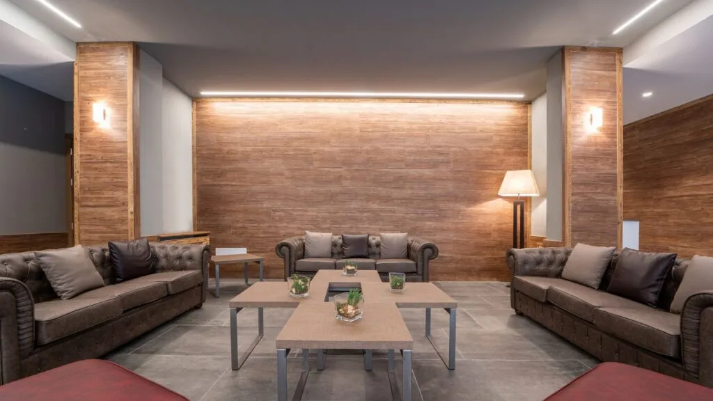 Interno elegante con divani in pelle, tavolini moderni e lampada, su sfondo di parete in legno chiaro. Ambiente accogliente.