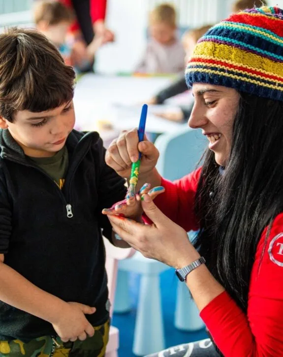 Animatrice sorridente intrattiene un bambino con attività creative al mini club
