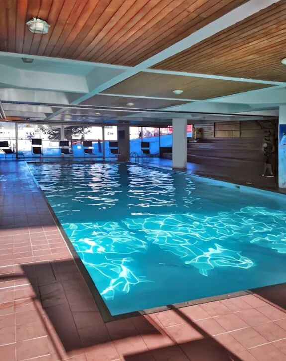 Piscina coperta con soffitto in legno e riflessi azzurri dell'acqua