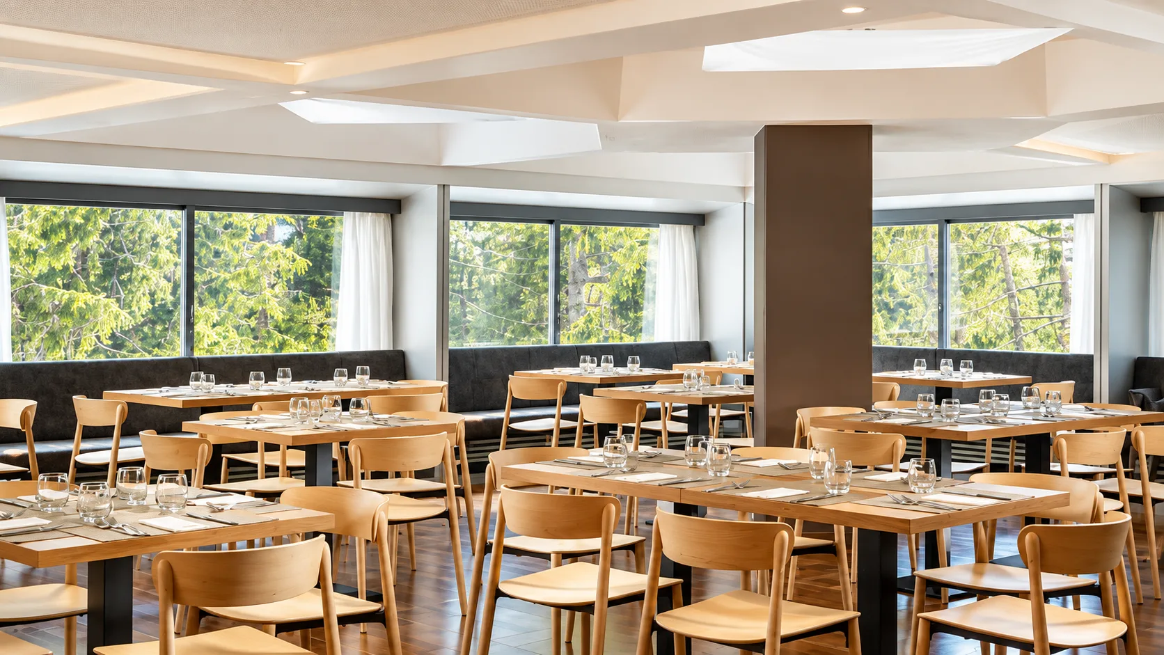 Sala ristorante luminosa con tavoli in legno e grandi vetrate sul bosco