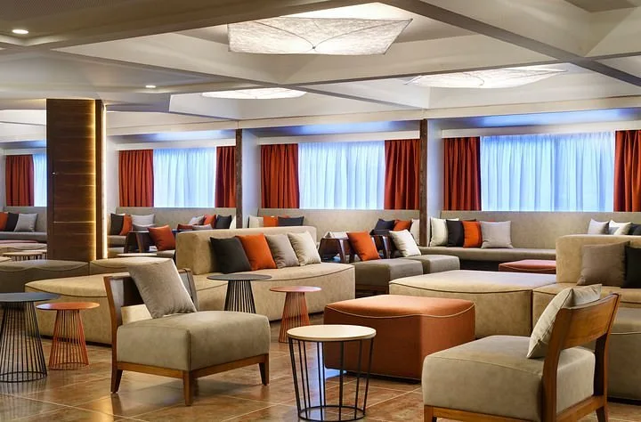 Ampia lounge con divani beige, cuscini colorati e tende arancioni