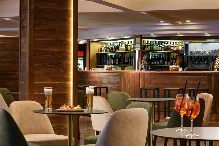 Bar dell'hotel con pareti in legno, bancone fornito e tavolini con aperitivi