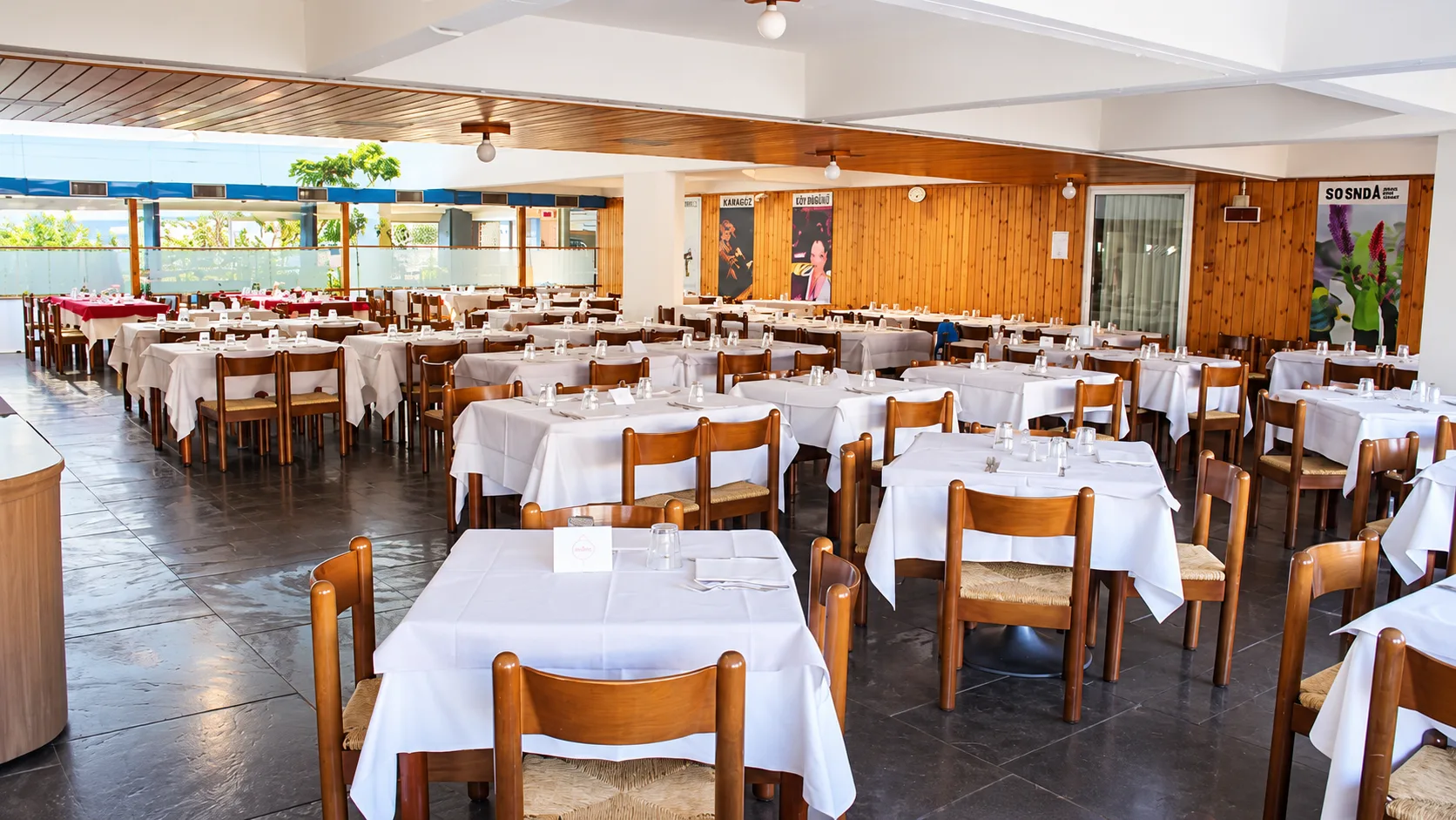 Sala da pranzo ampia con tavoli apparecchiati con tovaglie bianche e pareti in legno