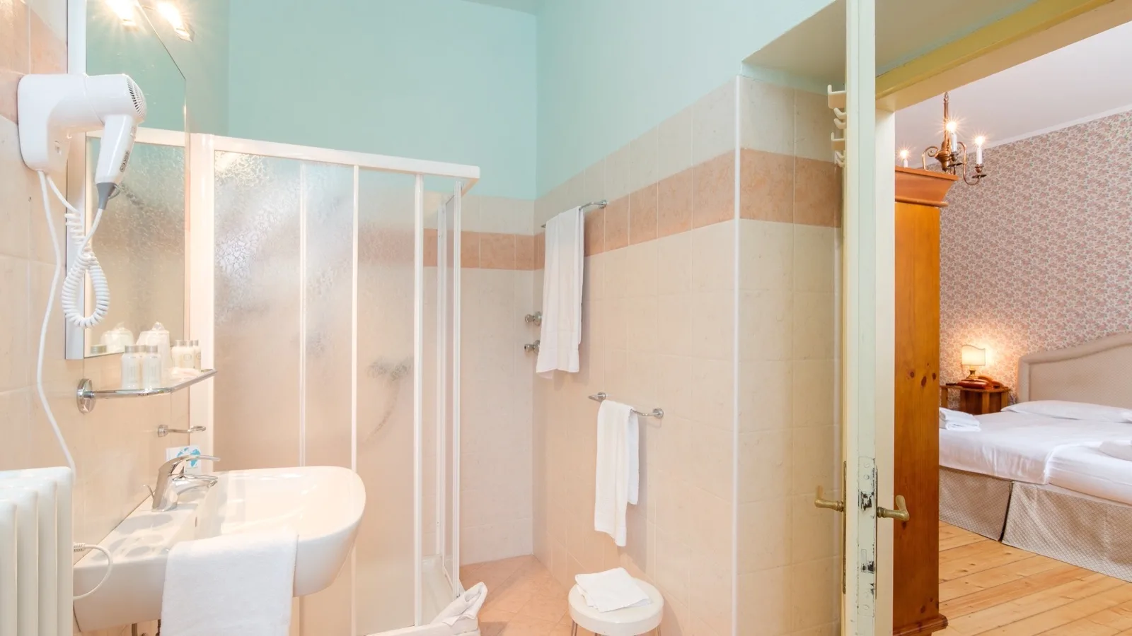 Bagno da hotel semplice con doccia, asciugacapelli, lavabo e accesso a camera da letto con letto matrimoniale.