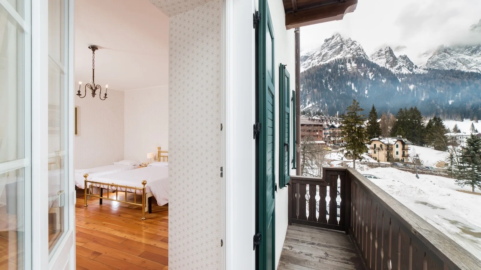 Balcone di legno con vista su paesaggio innevato e montagne, ingresso a camera con letti singoli e pavimento in legno.