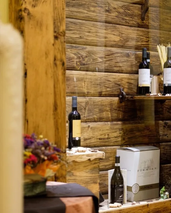 Vetrina rustica con bottiglie di vino, scatola di cartone e dettagli in legno naturale.