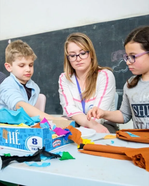 Bambini e insegnante impegnati in attività creativa con stoffe colorate in classe davanti a una lavagna.