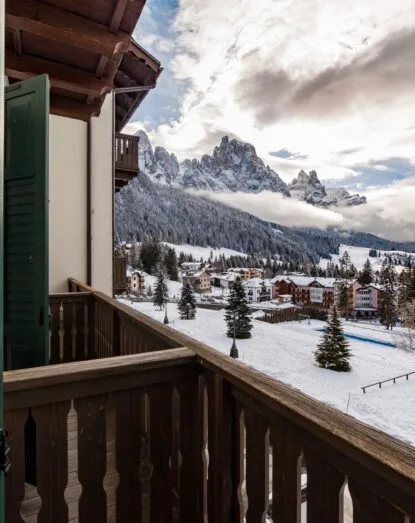 Balcone in legno con scorcio su villaggio innevato e montagna coperta di neve sotto cielo nuvoloso.