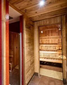 Ingresso a sauna in legno con porte di vetro e pareti rosse piastrellate accanto.
