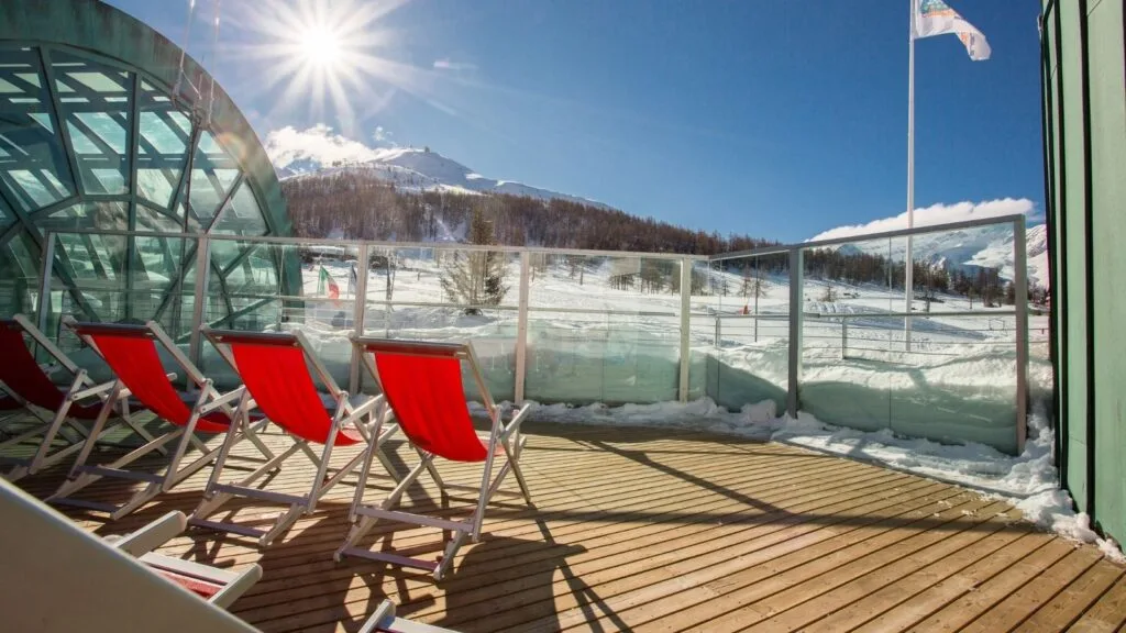 Terrazza in legno con lettini rossi affacciata sulle piste innevate