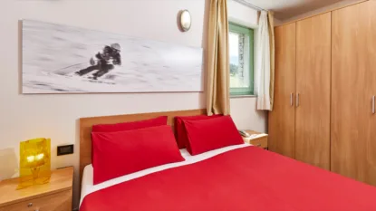 Camera da letto con letto matrimoniale rosso e quadro di sci