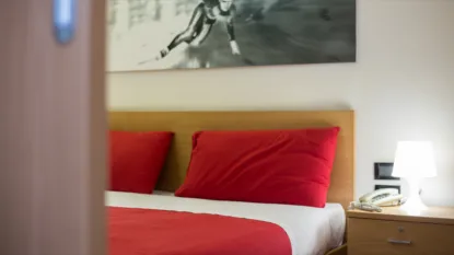 Dettaglio di letto matrimoniale con cuscini rossi e quadro sportivo