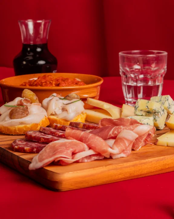 Tagliere di salumi e formaggi con bicchiere d'acqua su sfondo rosso