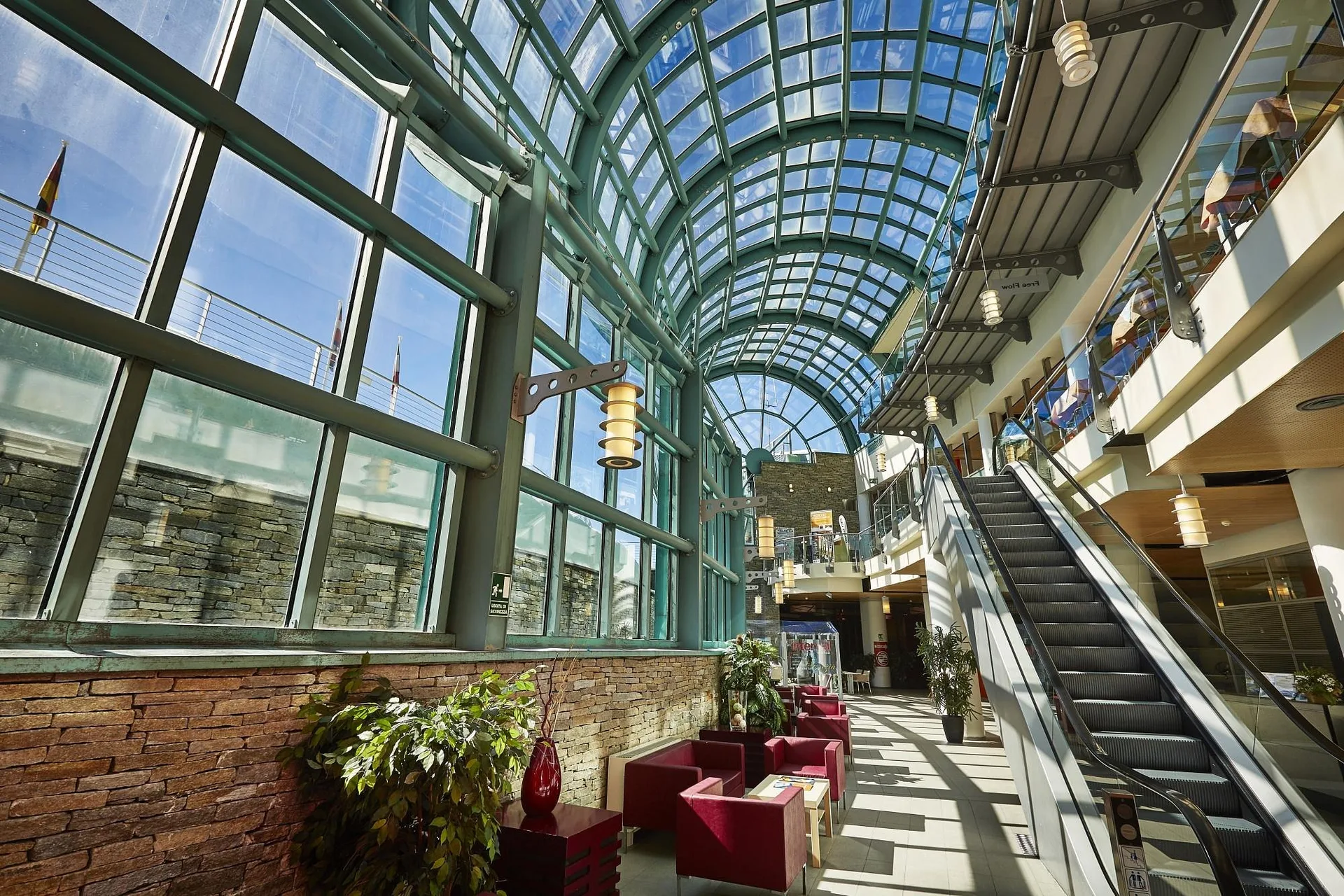Galleria interna con soffitto vetrato ad arco, poltrone rosse e scale mobili
