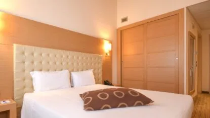 Camera da letto con letto matrimoniale, testiera imbottita beige e cuscino marrone con cerchi chiari.
