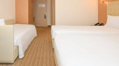 Camera d'albergo con due letti singoli e un divano letto, pavimento a righe e pareti beige chiare.