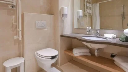 Bagno moderno con pareti beige, lavabo con specchio, asciugamani e water sospeso.