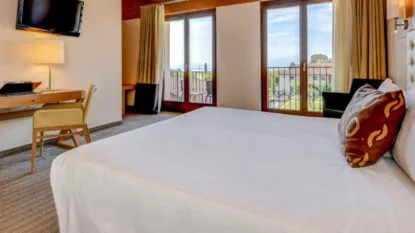 Camera da letto moderna con letto matrimoniale, scrivania, TV a muro e finestra con vista su balcone e giardino.