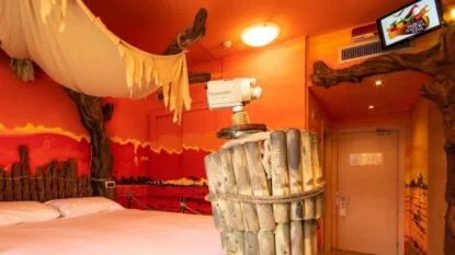 Camera tematica con pareti arancioni, letto matrimoniale e decorazioni safari, tra cui un proiettore vintage e dettagli di legno.