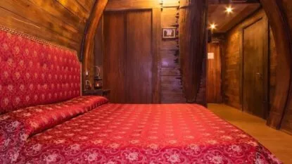 Camera accogliente con un letto rosso decorato, pareti in legno e illuminazione calda, crea un'atmosfera rustica e intima.
