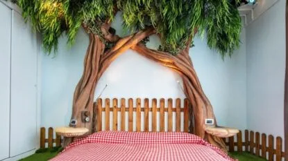 Letto con testiera a forma di albero, decorato con foglie e un copriletto a quadratini rossi, in una stanza moderna.