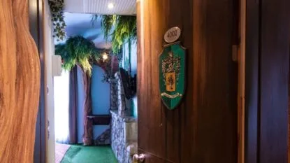 Ingresso a una stanza d'albergo con porta in legno, numero 4002, e decorazioni di piante all'interno del corridoio.