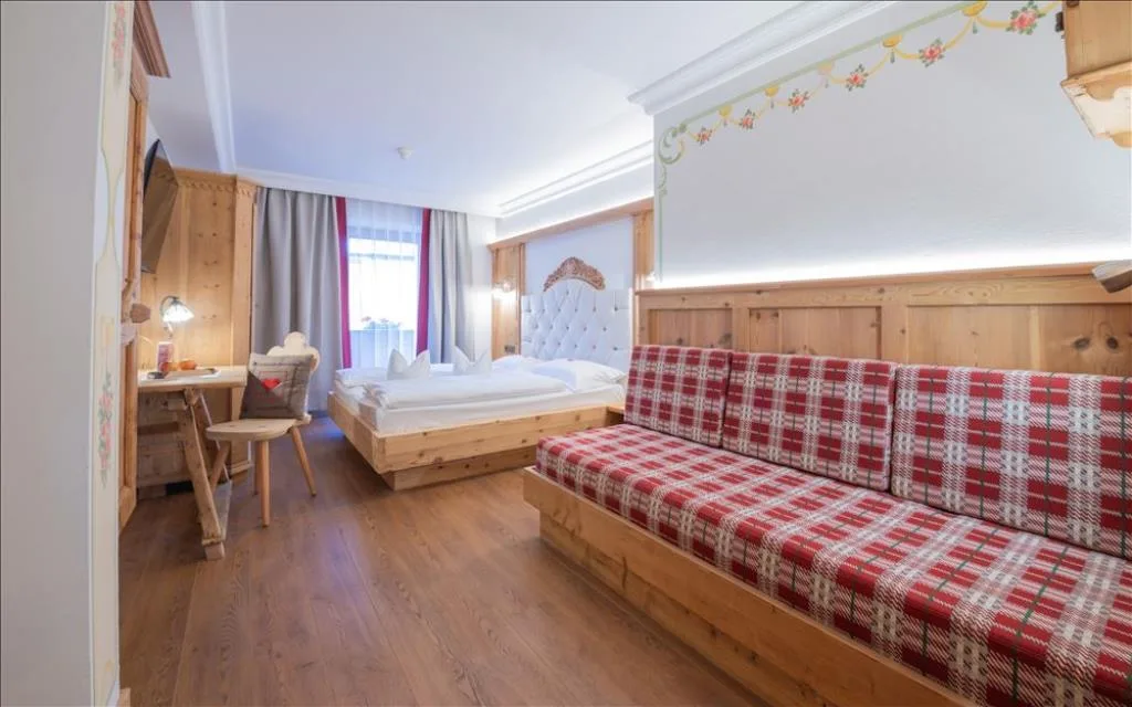 Camera ampia con letto in legno, divano a scacchi rossi e decori dipinti