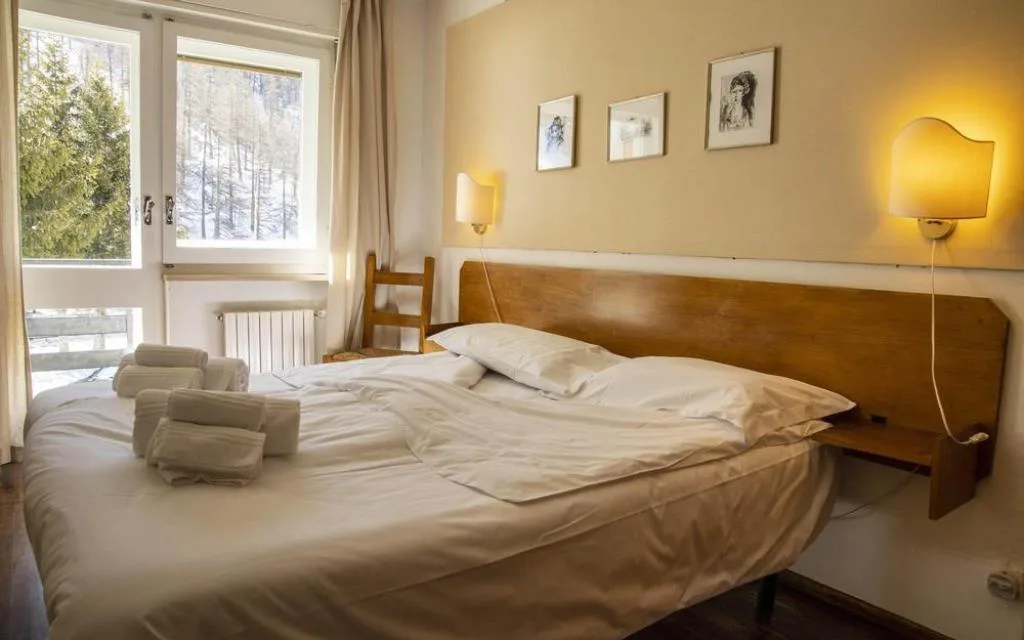 Camera luminosa con letto matrimoniale, finestra con vista sul bosco e quadri alle pareti